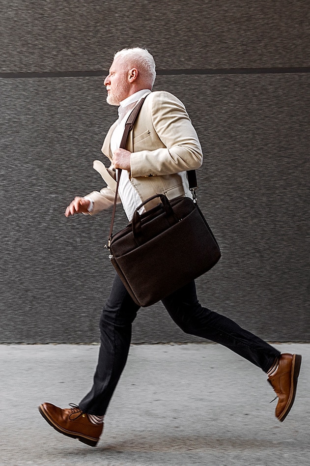 Man in a blazer hurrying along the street with a work bag