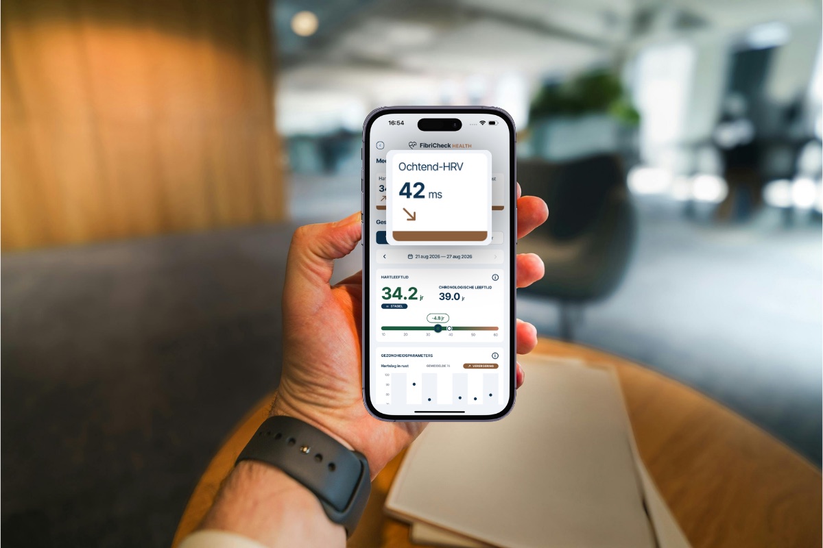 Iemand houdt een telefoon vast met het FibriCheck Health-scherm open, met een ochtend-HRV van 42 ms, boven een hartleeftijd van 34,2 jaar en een grafiek van de hartslag in rust.